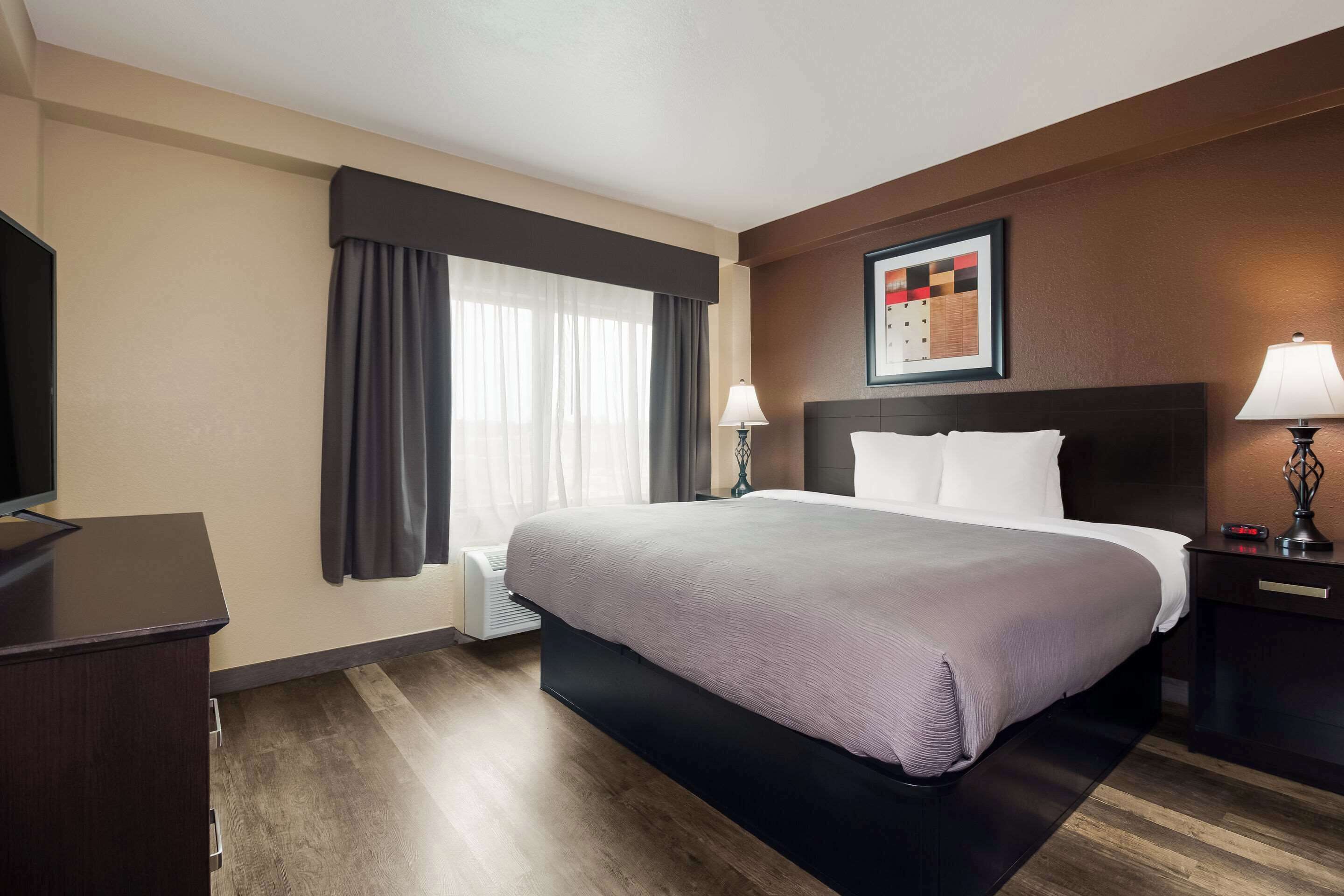 A hotel room with a large bed, a desk, a TV, and a window with curtains.