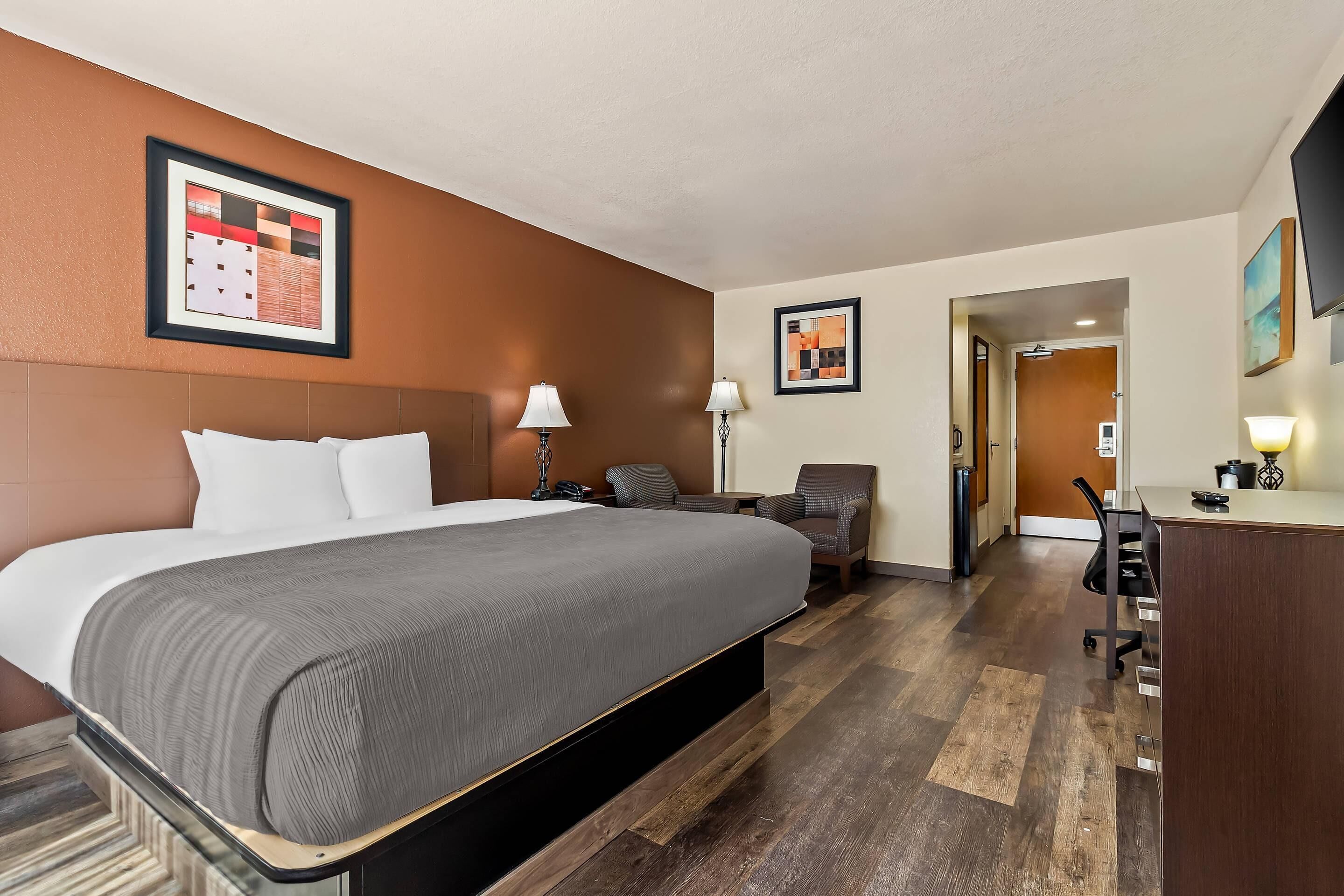 A hotel room with a large bed, a desk, a chair, and a television.
