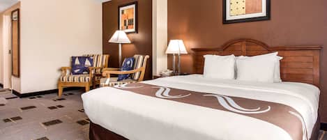 A hotel room with a large bed, two chairs, a desk, and a lamp.