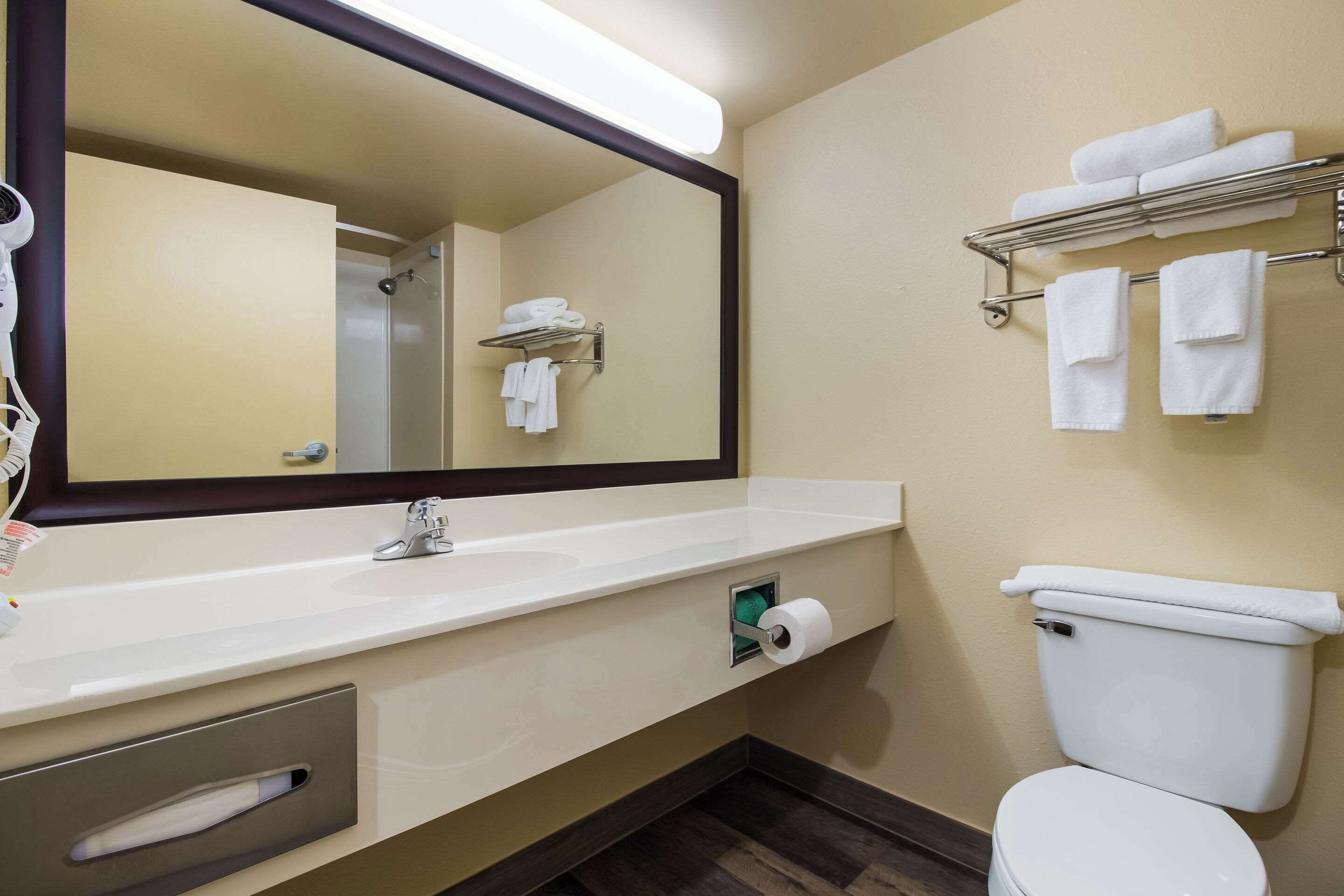 A bathroom with a large mirror, a toilet, a towel rack, and a sink with a towel dispenser.