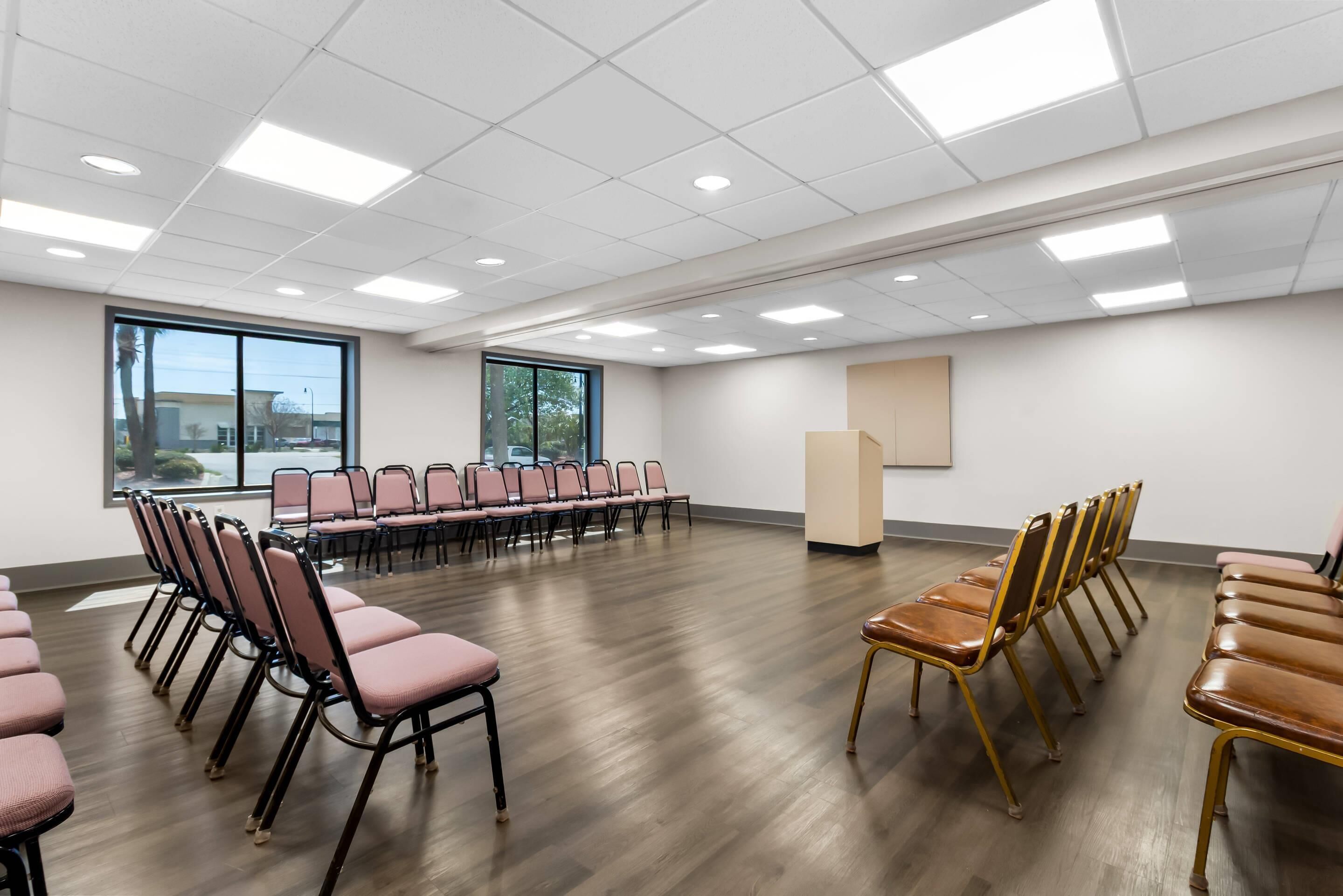 A conference room with rows of chairs, large windows, and a wooden floor.