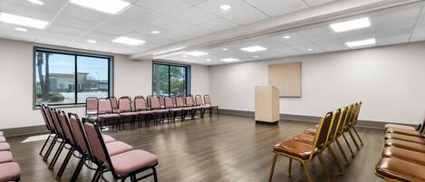 A conference room with rows of chairs, large windows, and a wooden floor.