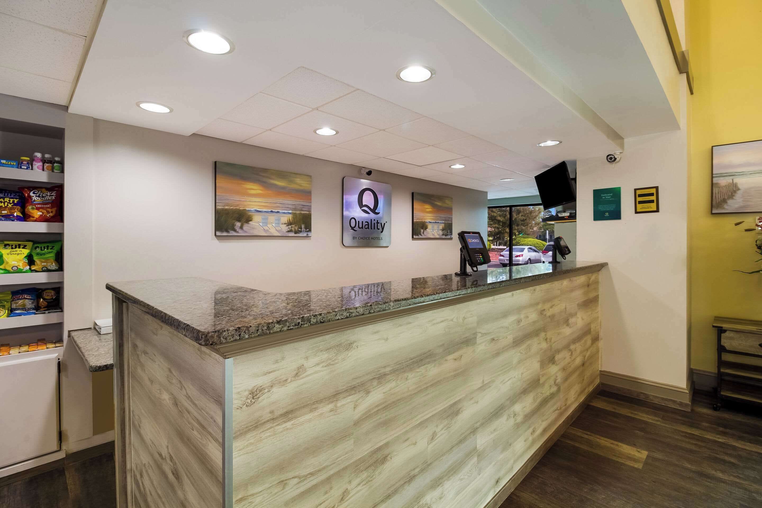 Un'area reception di un hotel con un bancone in marmo, un cartello con la scritta 'Quality' e il logo 'By Choice Hotels'.