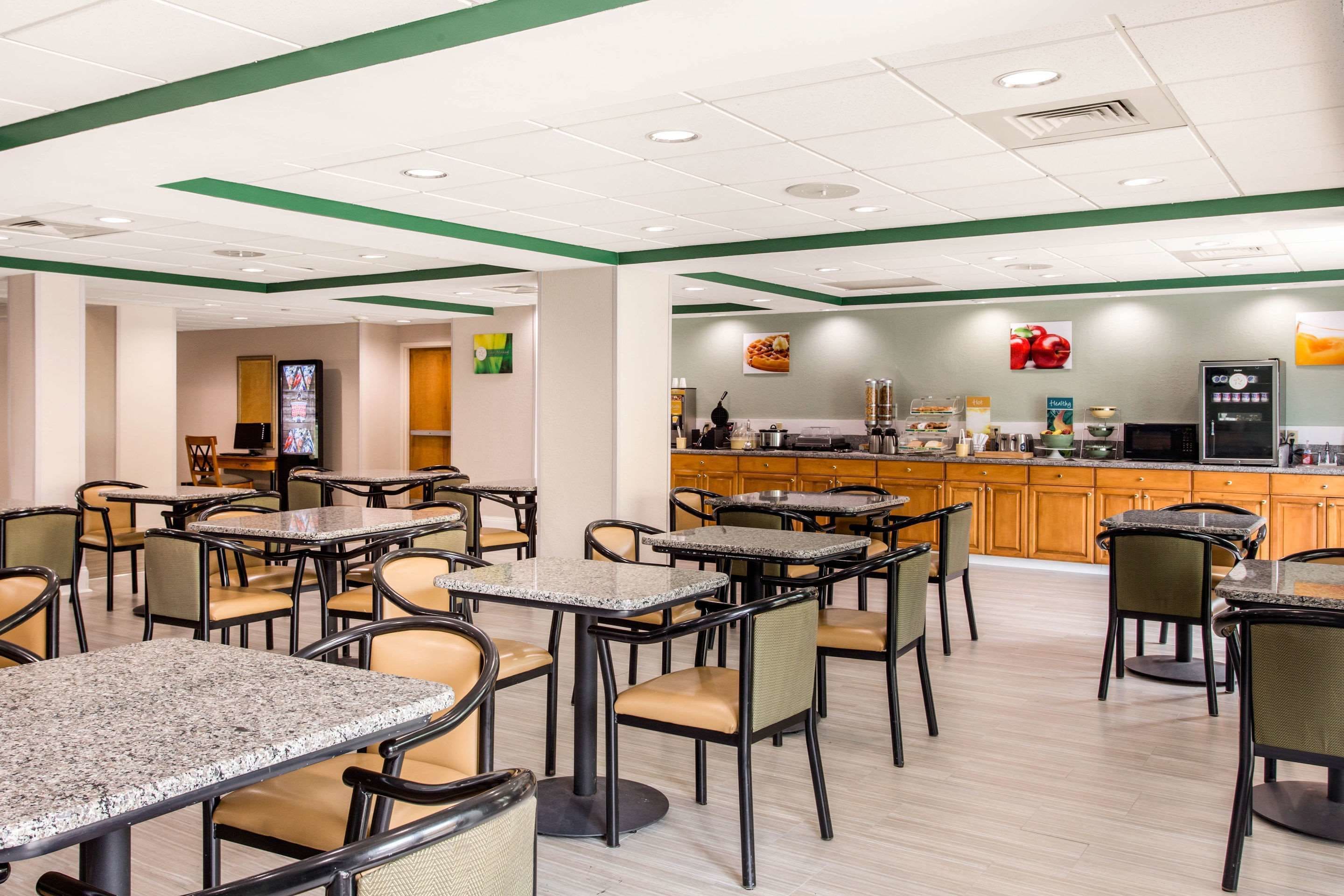 A restaurant with multiple tables and chairs, a kitchen area, and a counter with a beverage dispenser.