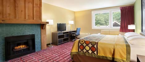 Habitación de hotel con chimenea, cama con colcha estampada, escritorio con computadora y ventana con cortinas.