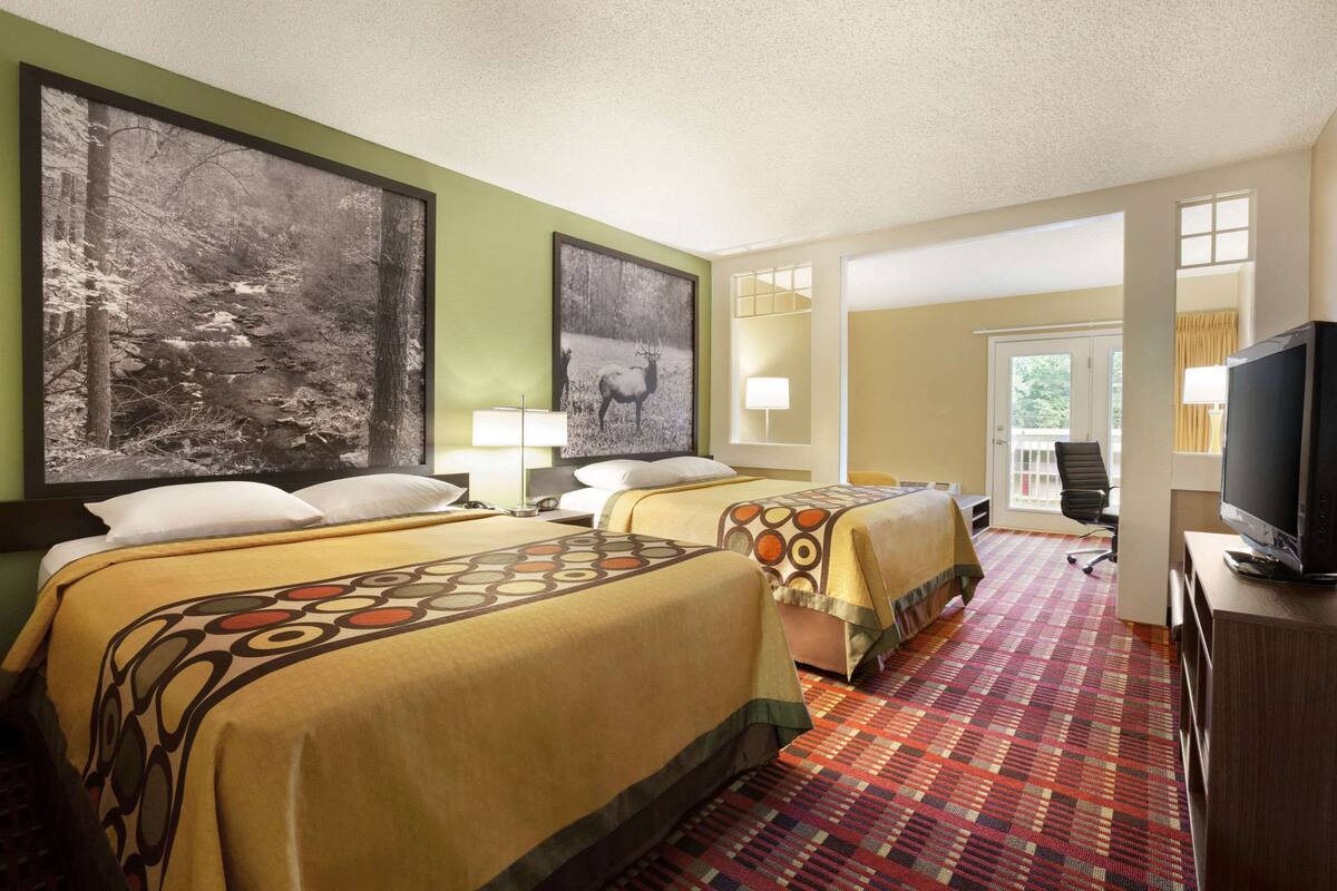A hotel room with two beds, a television, a desk, and a large window.