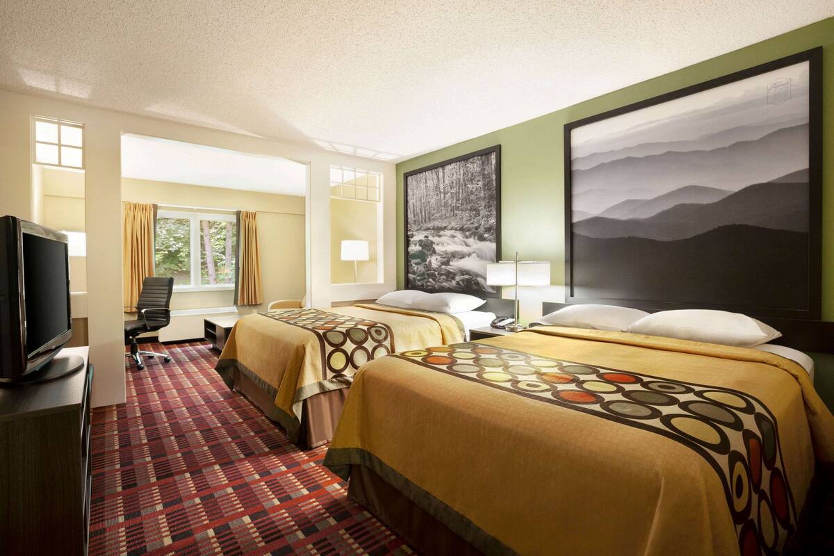 A hotel room with two beds, a TV, a desk, and a window with curtains.