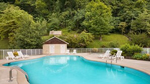A swimming pool with a small building in the background, surrounded by trees. - Super 8 by Wyndham Cherokee (Cherokee)