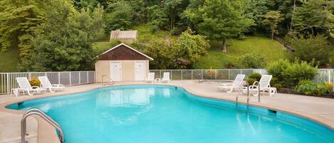 A swimming pool with a small building in the background, surrounded by trees.