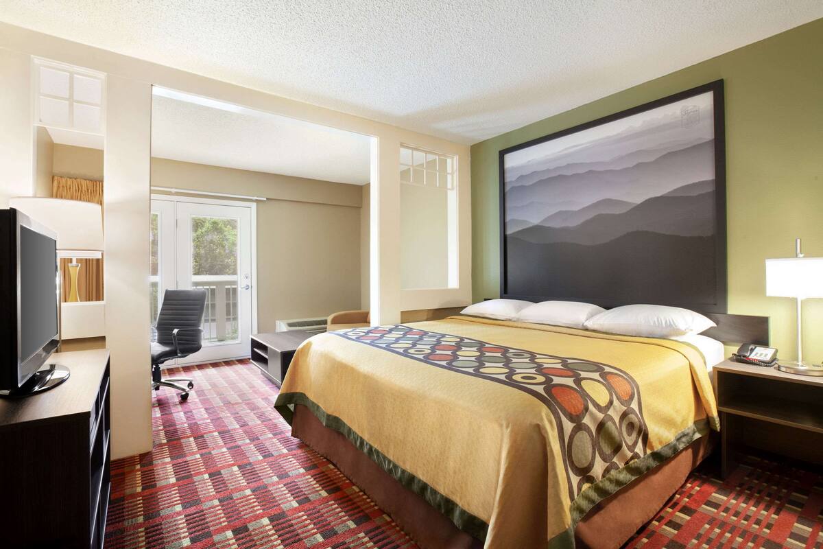 A hotel room with a bed, a desk with a computer, a chair, a TV, and a large window.