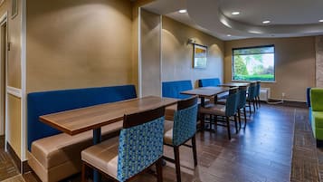 A restaurant with wooden tables and blue cushioned booths, a large window with a view of greenery, and a ceiling with recessed lighting.