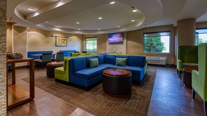 A modern lounge area with a sectional sofa, round coffee tables, and a TV mounted on the wall. - Comfort Inn Shepherdsville - Louisville South (Louisville)