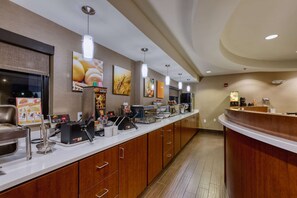 A hotel reception area with a long counter, wooden cabinets, and various amenities like a coffee machine and a food display.