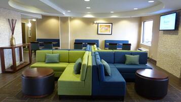 A modern lounge area with sectional sofas in green and blue, two round wooden tables, and a framed picture on the wall.