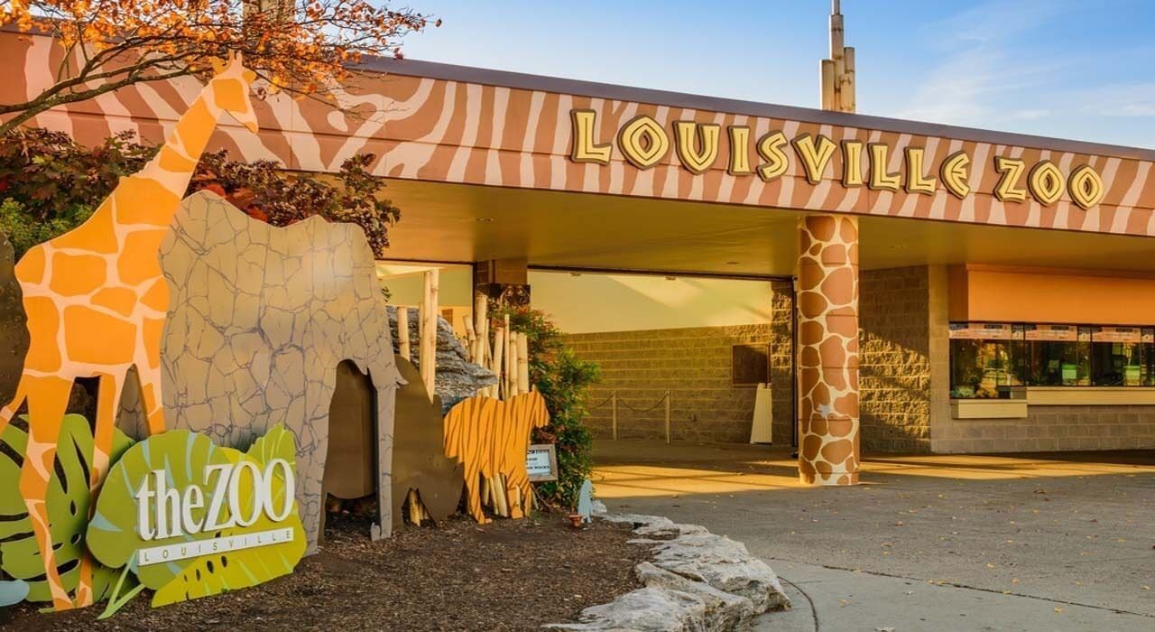 The entrance to the Louisville Zoo with a giraffe sculpture and a sign.