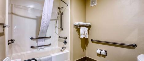 A bathroom with a bathtub, a toilet, a shower with a grab bar, a wheelchair-accessible chair, and a towel rack.