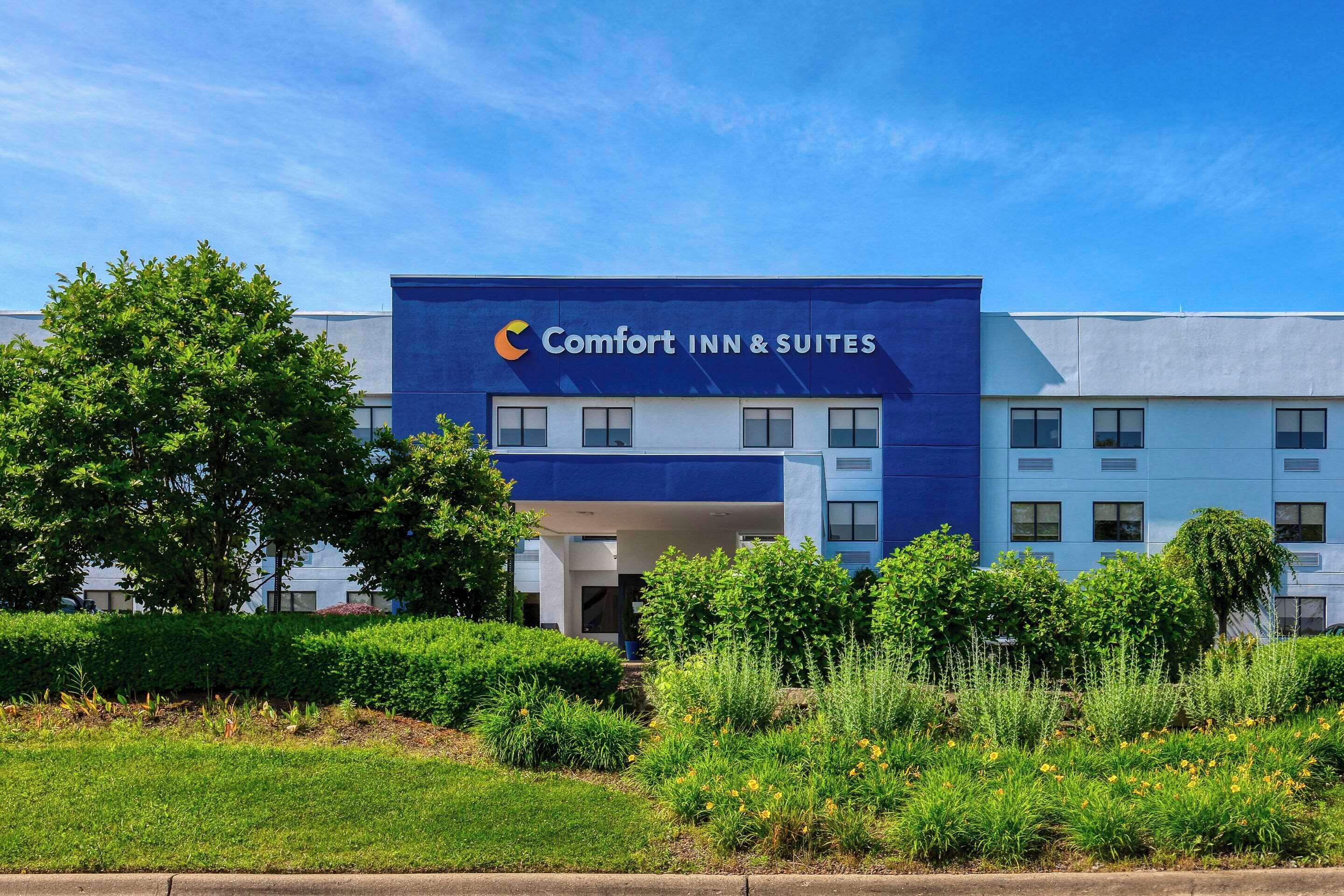 Un hotel Comfort Inn & Suites con fachada moderna, múltiples ventanas y un jardín bien cuidado al frente.
