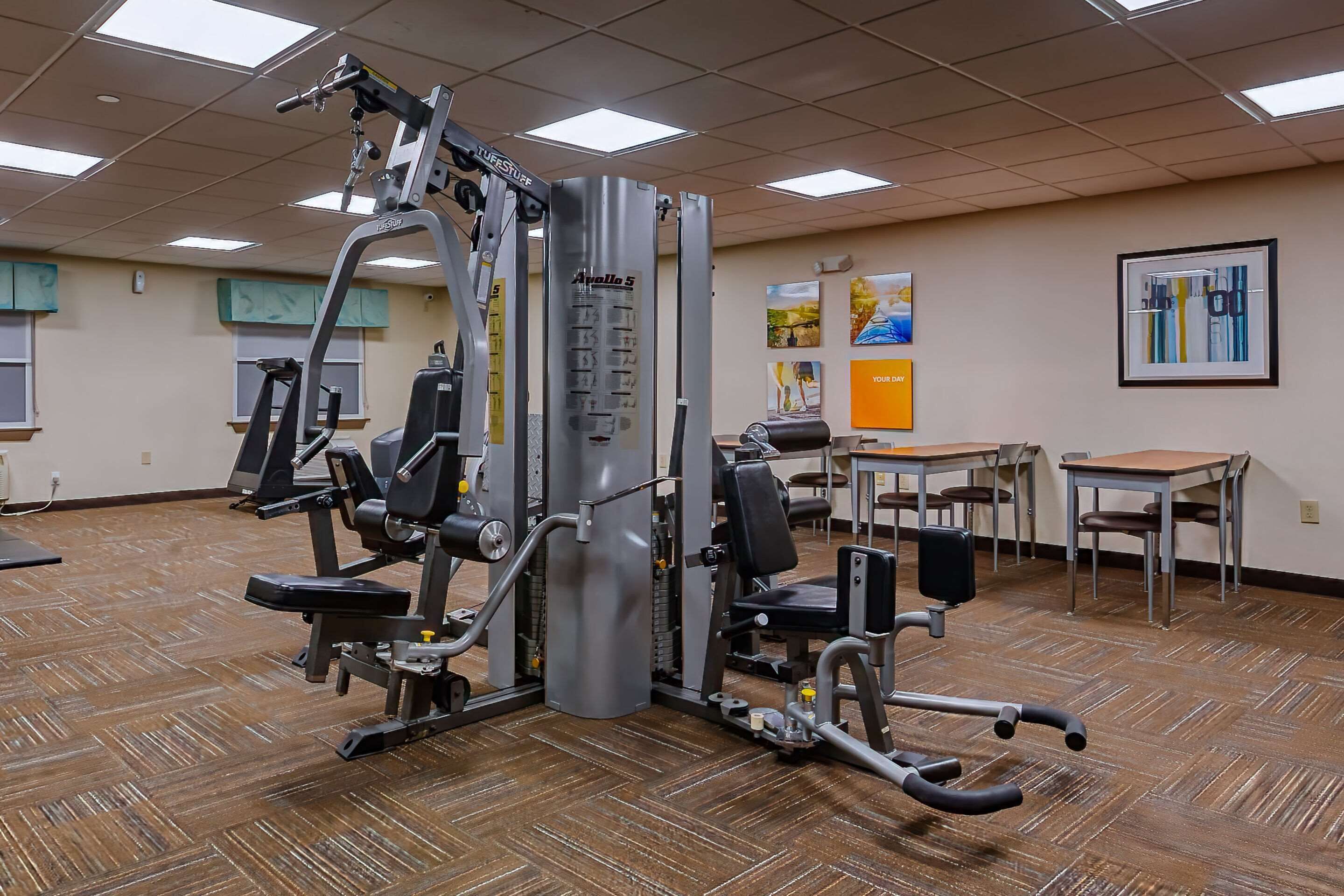 A gym with various exercise machines, a wooden floor, and a table with chairs.