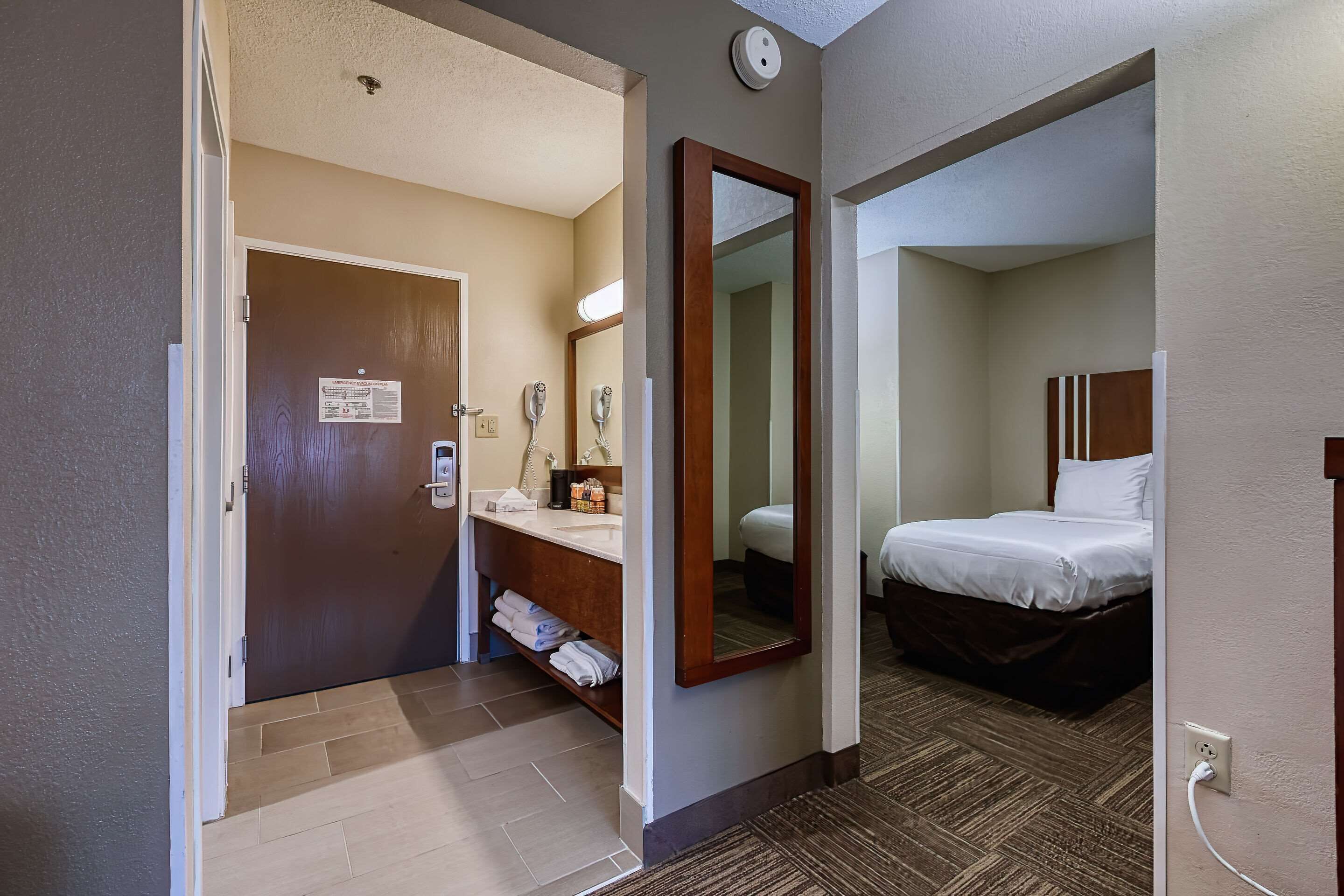 A hotel room with a bed, a bathroom with a sink and mirror, and a door leading to another room.