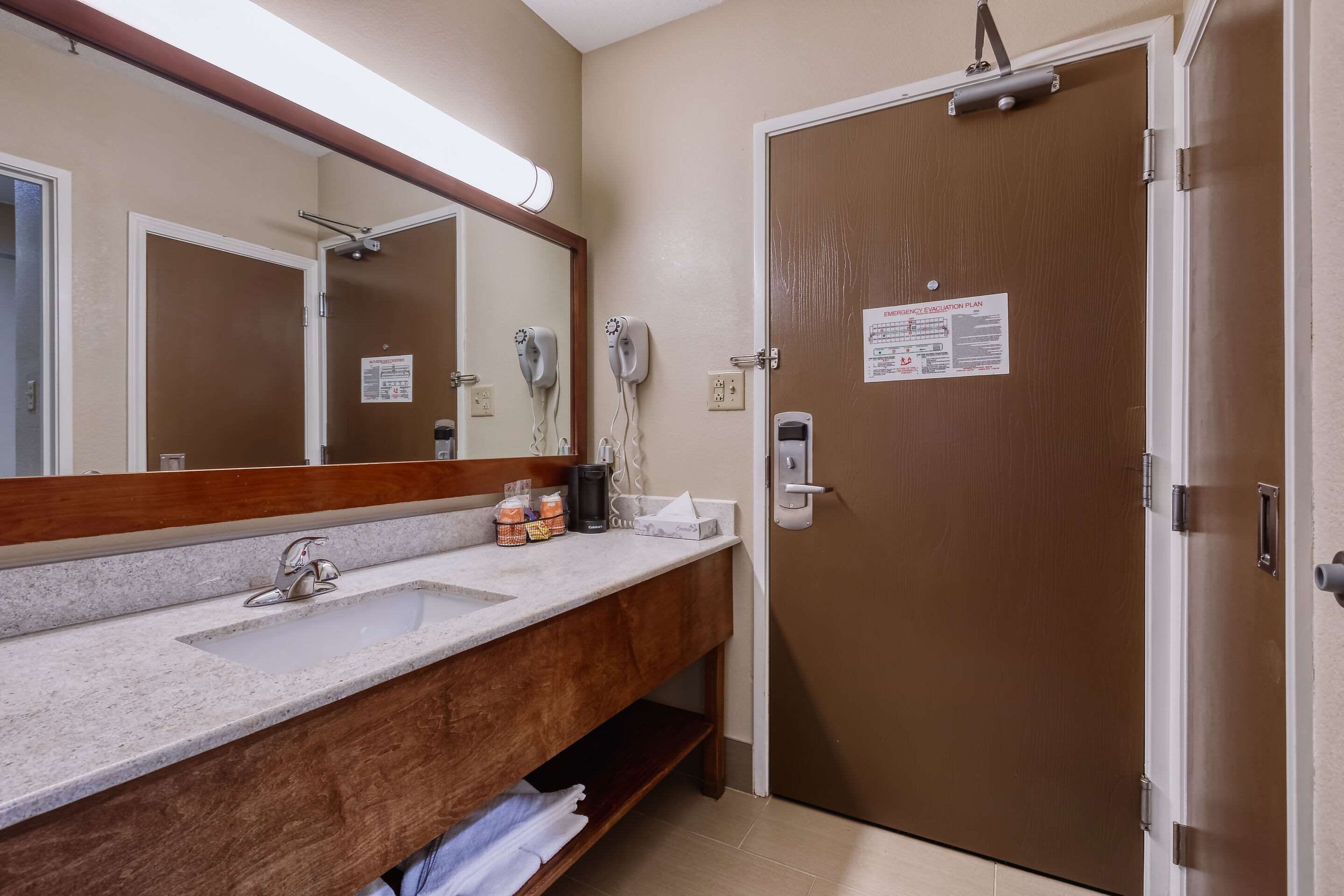 A bathroom with a sink, mirror, and towel rack. There is a door with a sign on it.
