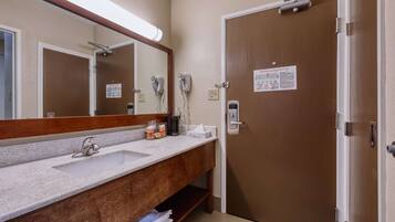 A bathroom with a sink, mirror, and towel rack. There is a door with a sign on it.