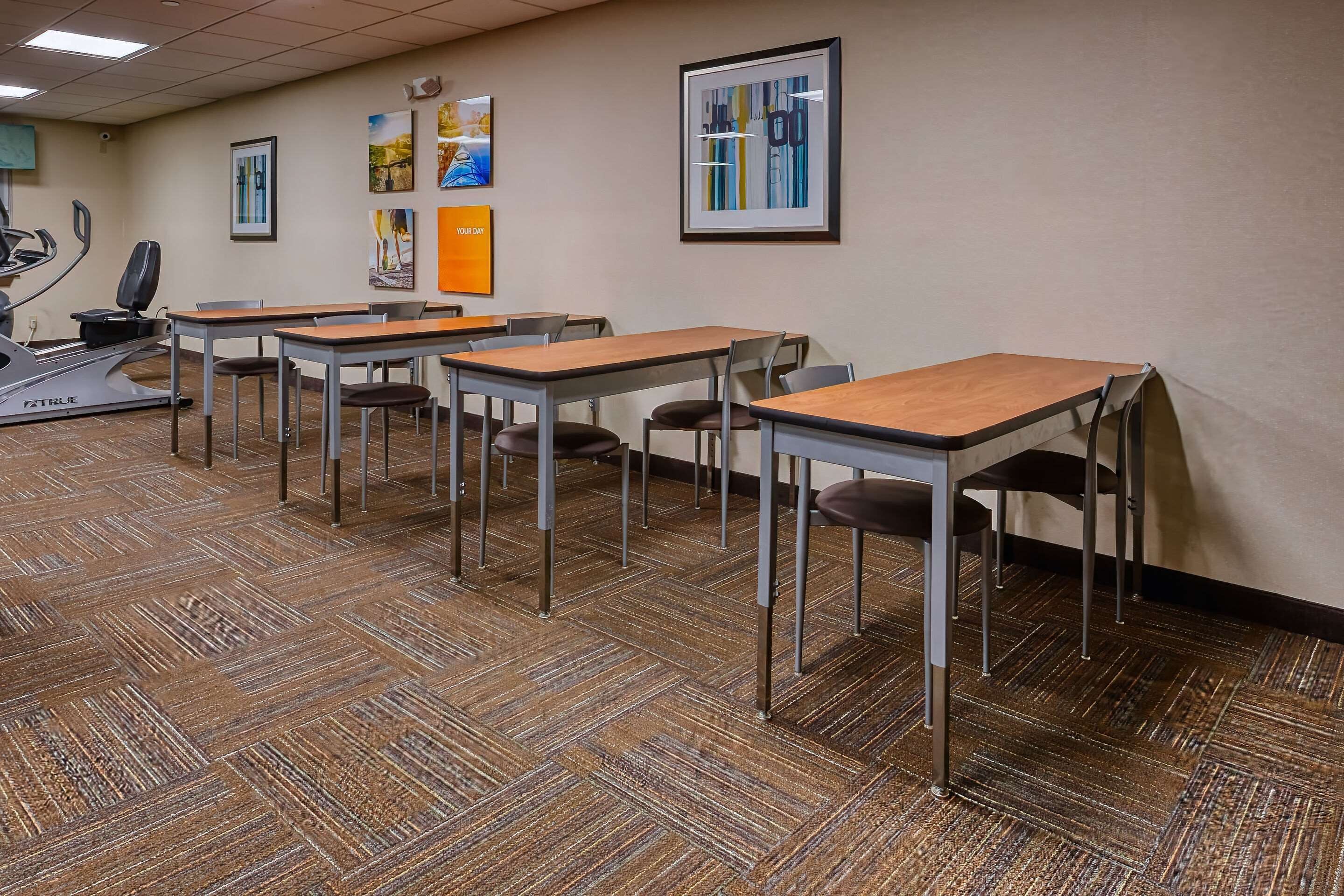 A conference room with multiple tables and chairs, a treadmill, and framed artwork on the walls.