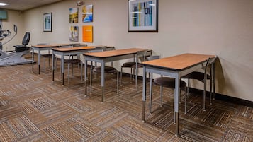 A conference room with multiple tables and chairs, a treadmill, and framed artwork on the walls.
