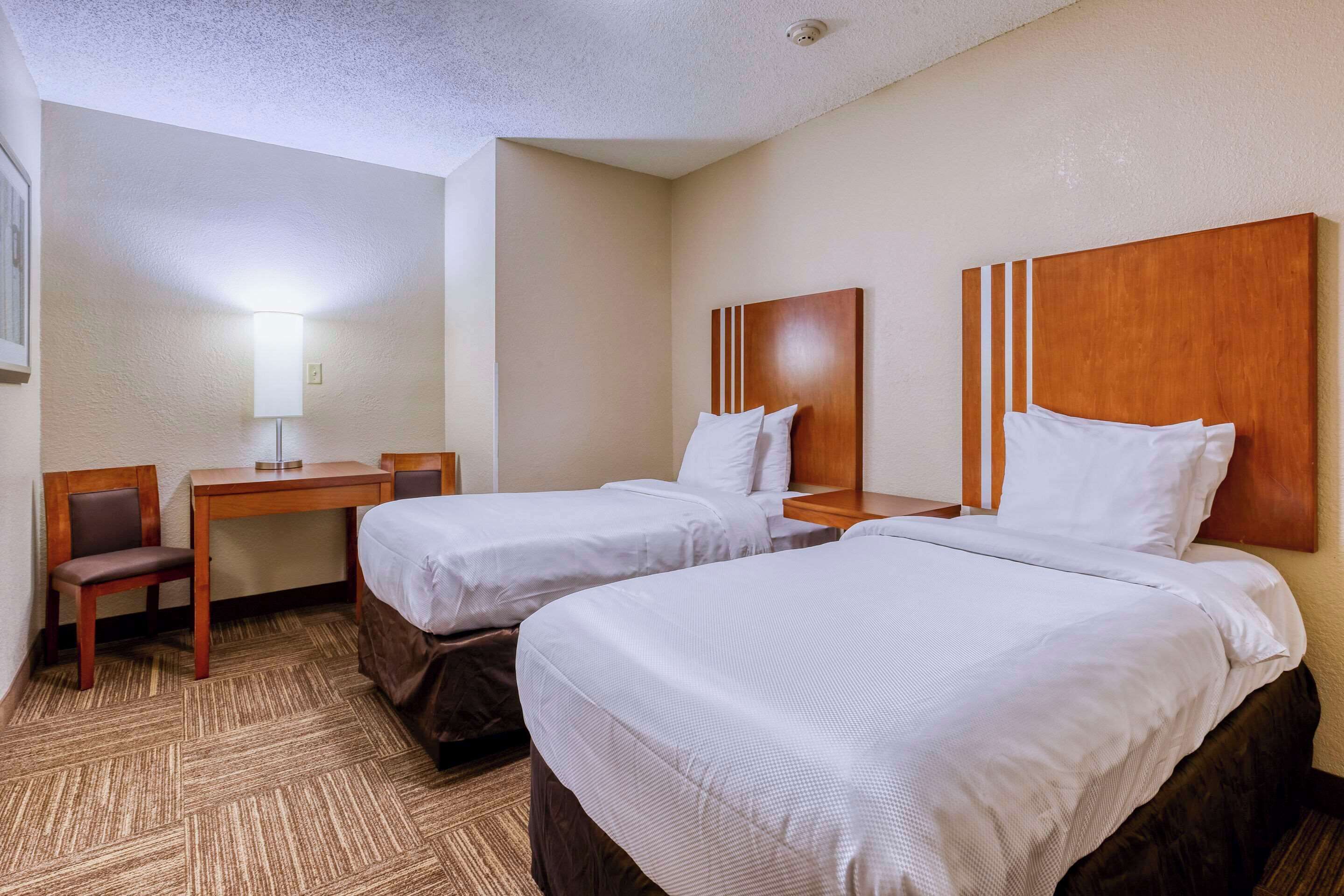 A hotel room with two beds, a desk, and a chair.