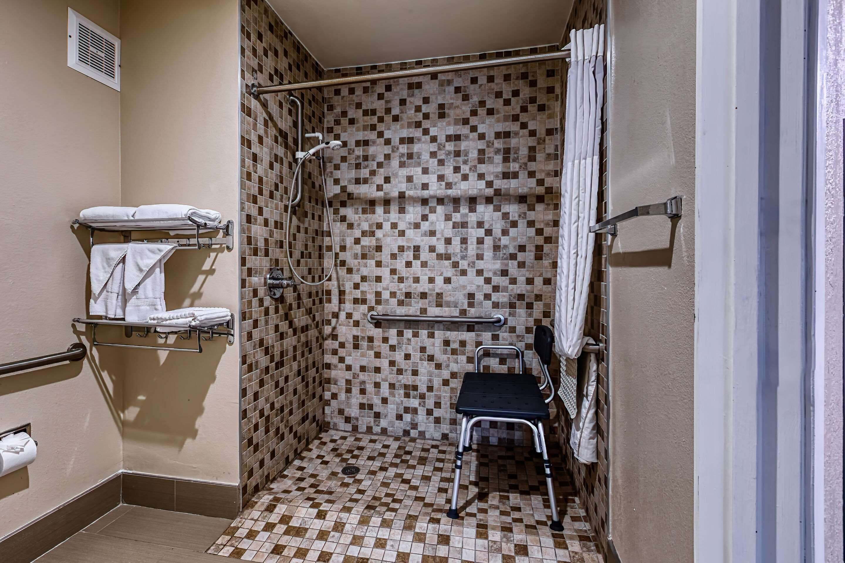 A small, tiled shower area with a shower chair, a towel rack, and a handrail.
