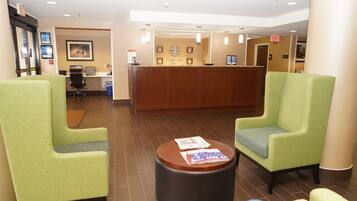 A hotel lobby with green armchairs, a reception desk, and a small round table with magazines.