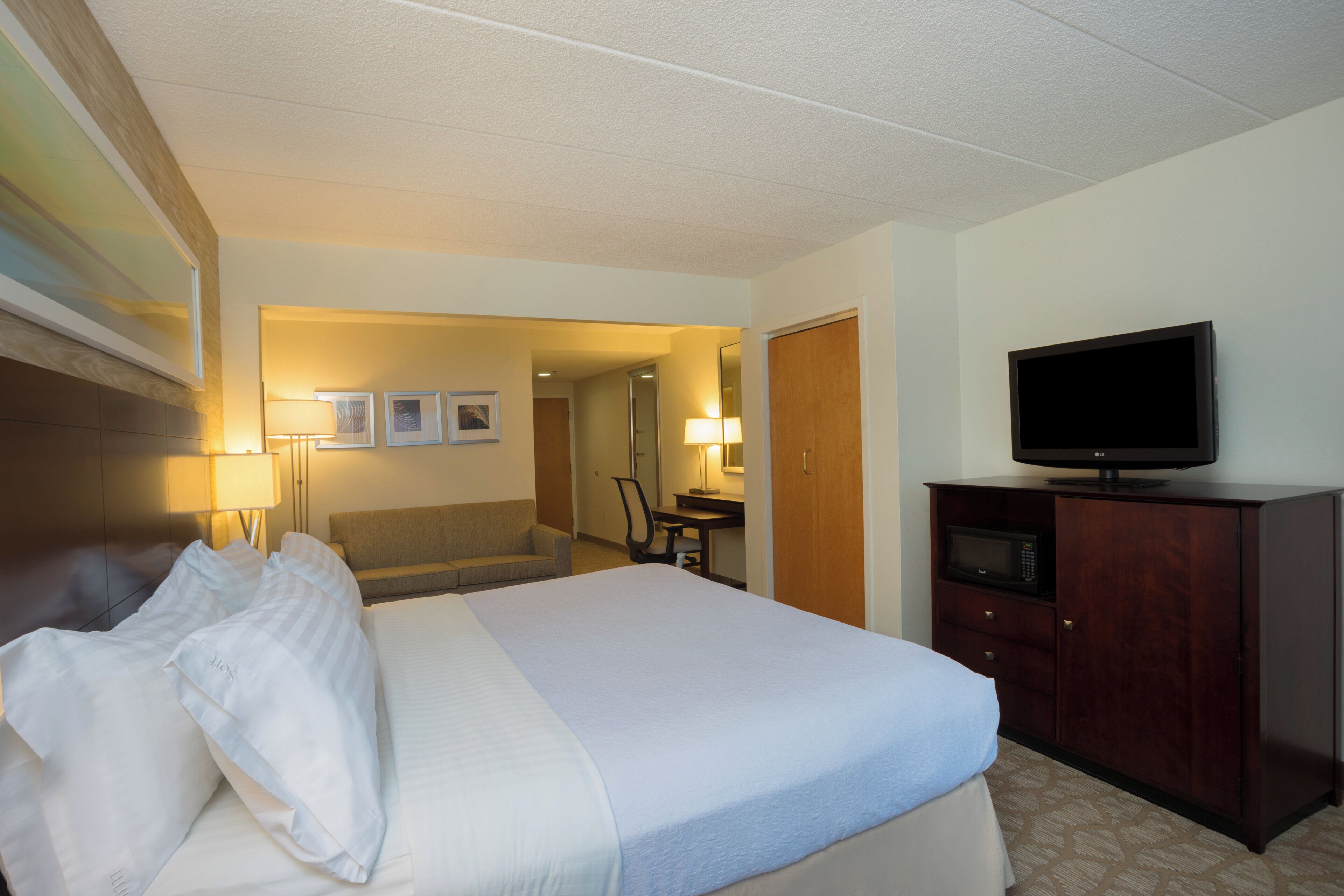 Una habitación de hotel con cama, escritorio, televisor y armario.