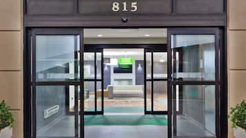 A hotel entrance with a glass door, a number '815' above, and a green mat at the entrance.