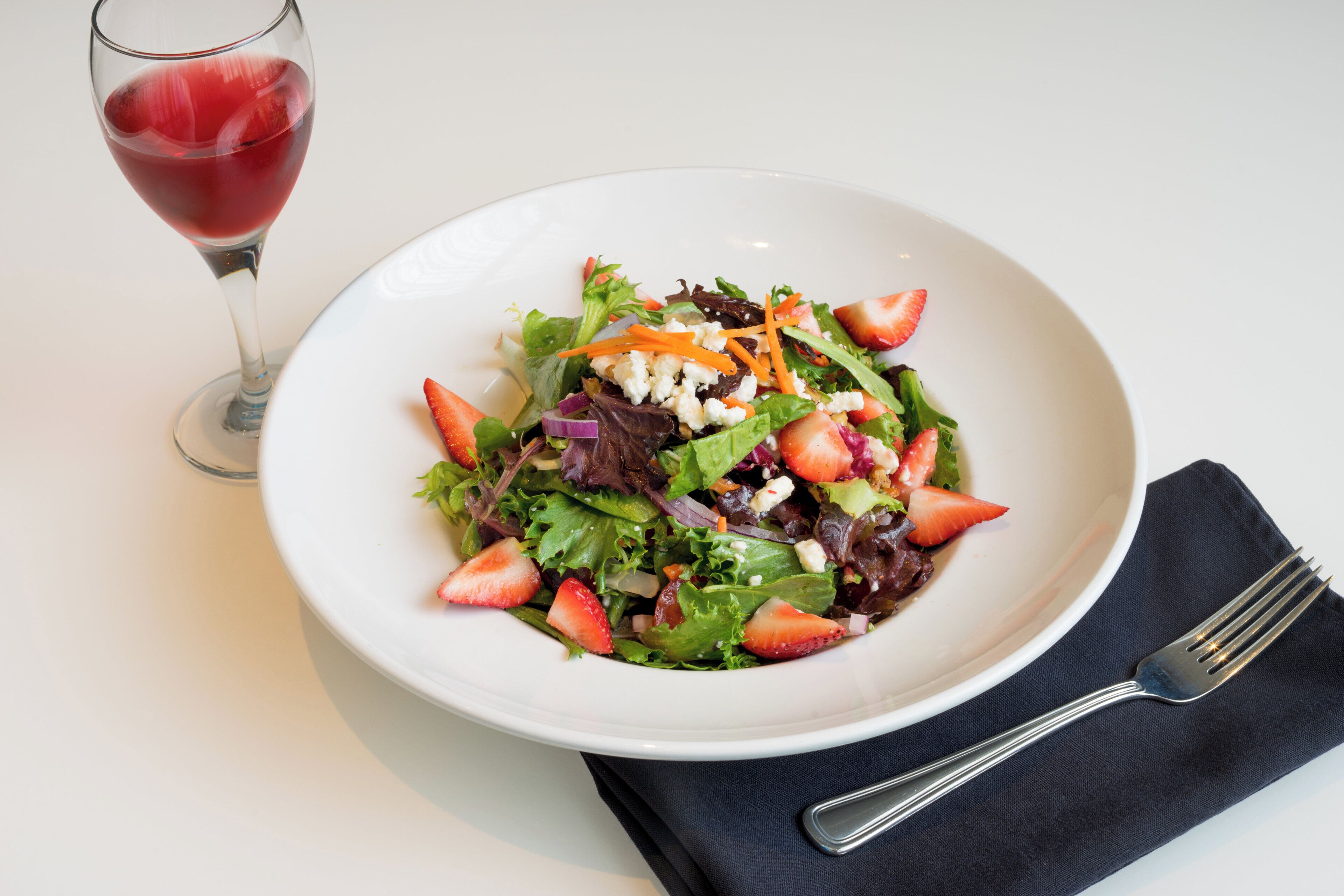 A white plate with a salad, a glass of red wine, and a fork on a napkin.