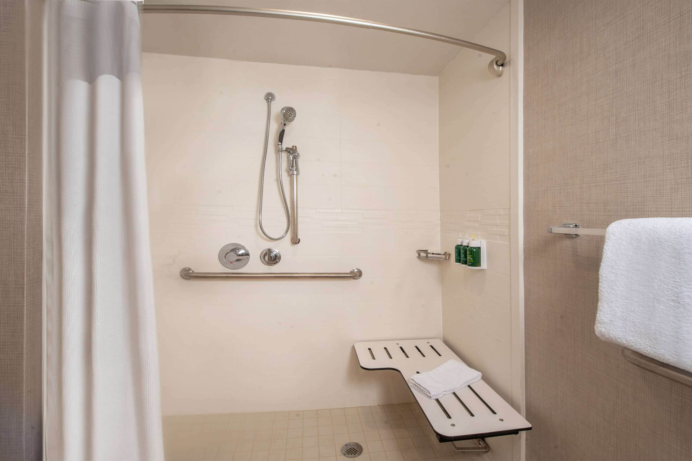 A shower area with a handheld showerhead, a towel rack, and a grab bar.