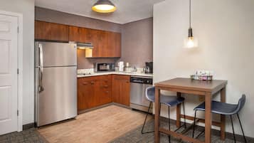 A compact kitchen with wooden cabinets, stainless steel appliances, a microwave, and a dishwasher. There is a small dining table with two chairs.