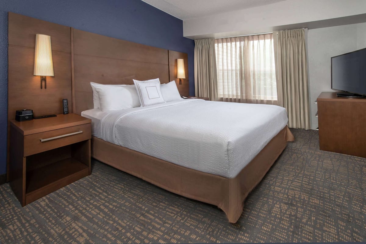 A hotel room with a large bed, a nightstand, a TV, and a window with curtains.