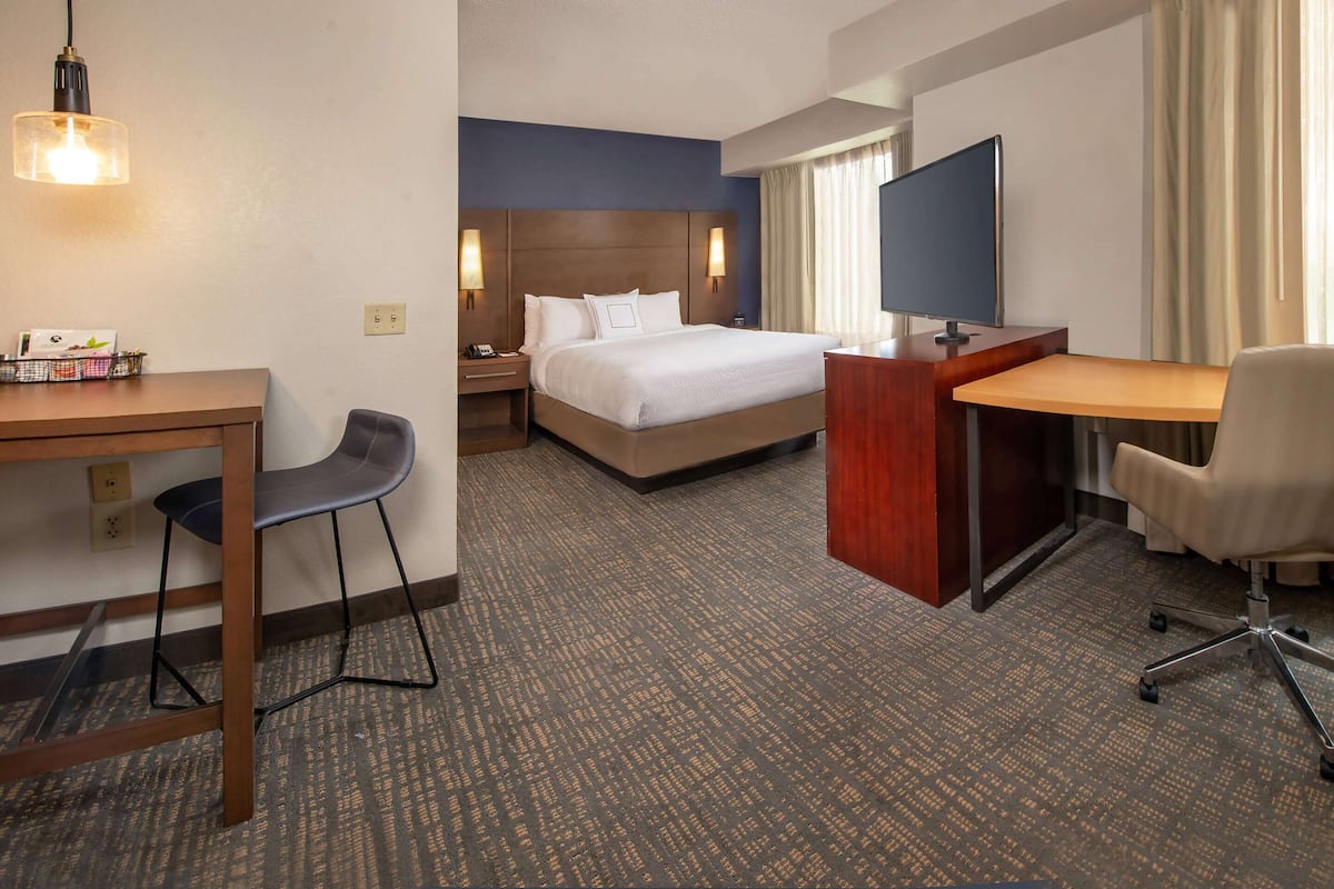 A hotel room with a bed, desk, chair, TV, and a desk lamp.