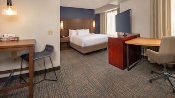 Una habitación de hotel con cama, escritorio, silla, televisor y lámpara de escritorio.