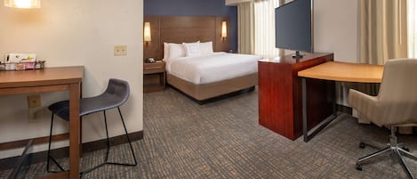 A hotel room with a bed, desk, chair, TV, and a desk lamp.