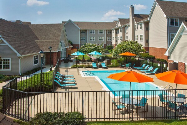 A swimming pool area with lounge chairs and umbrellas, surrounded by a fence.
