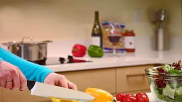 A kitchen with a person slicing a yellow bell pepper on a cutting board, a bowl of salad, and various kitchen items in the background.