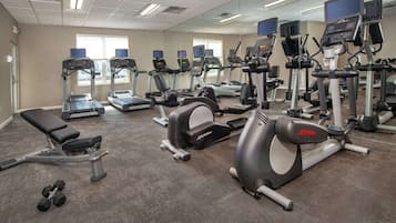 A gym with various exercise machines, a bench, and dumbbells.
