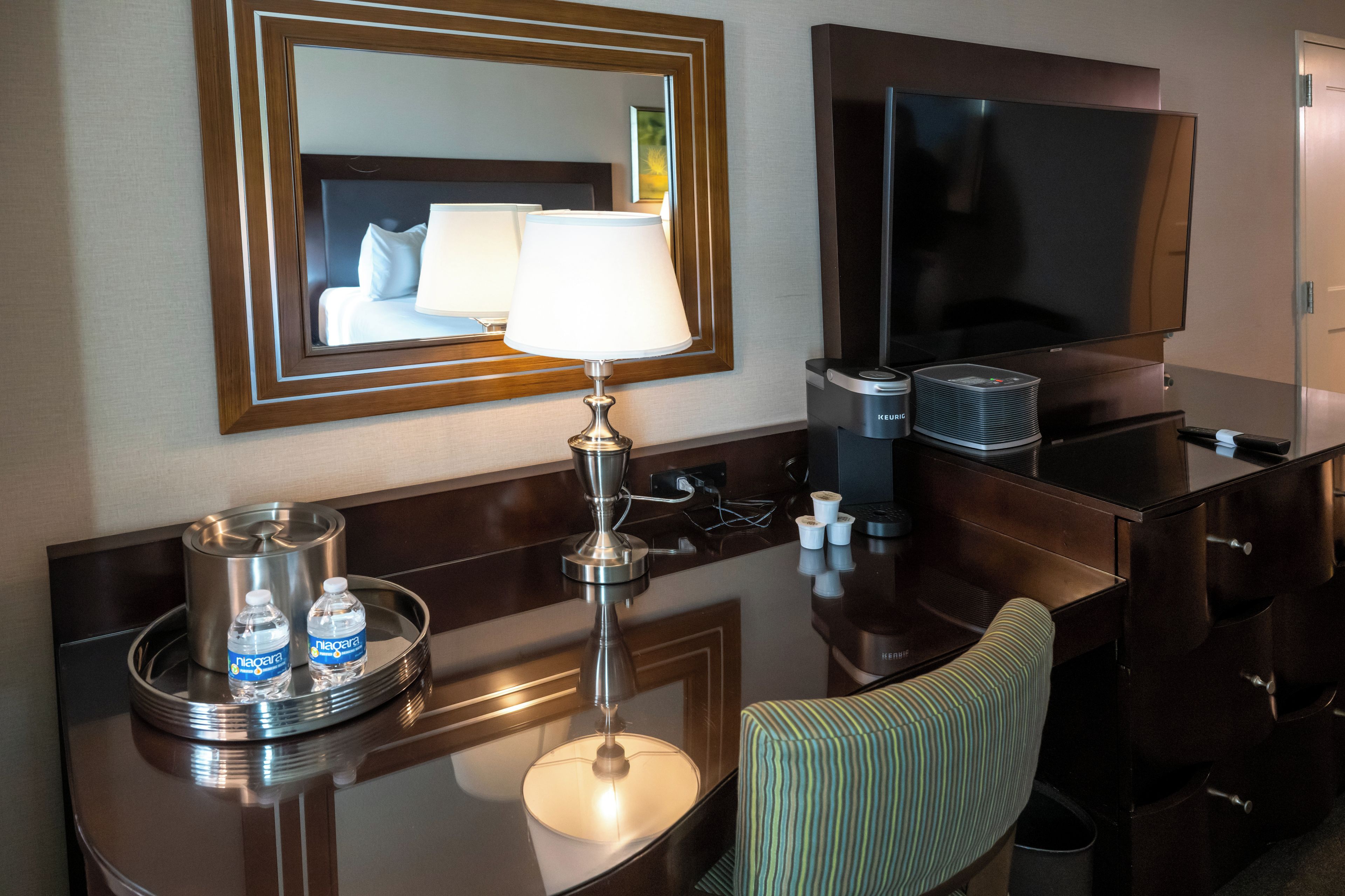 Une chambre d’hôtel équipée d’un bureau, d’un miroir, d’une télévision, d’une lampe et d’une chaise.