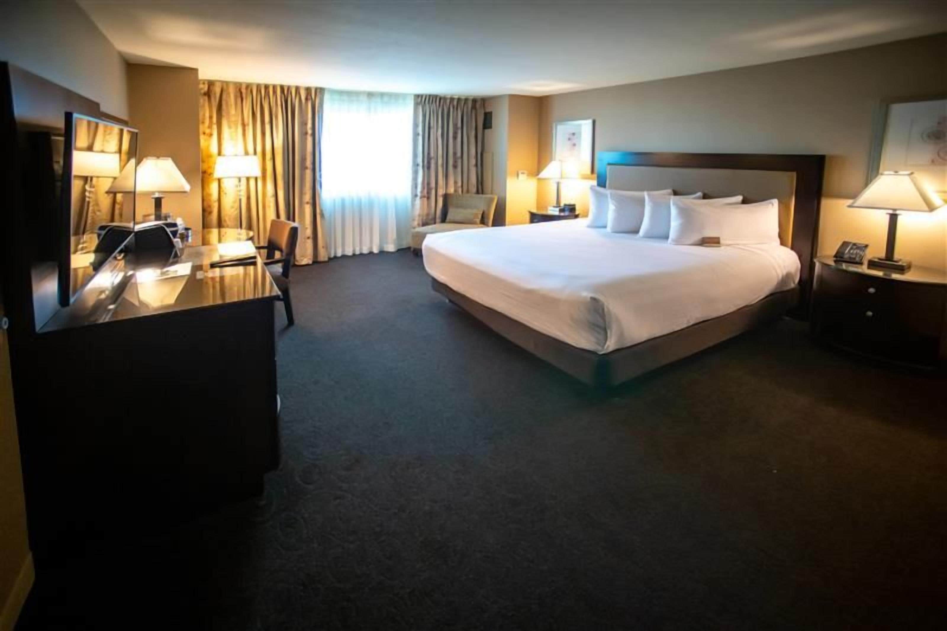 A hotel room with a large bed, a desk, a chair, and two bedside tables with lamps.