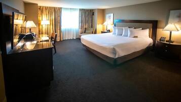 A hotel room with a large bed, a desk, a chair, and two bedside tables with lamps.