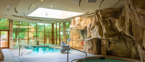 An indoor swimming pool with a rocky wall backdrop, clear glass windows, and a skylight.