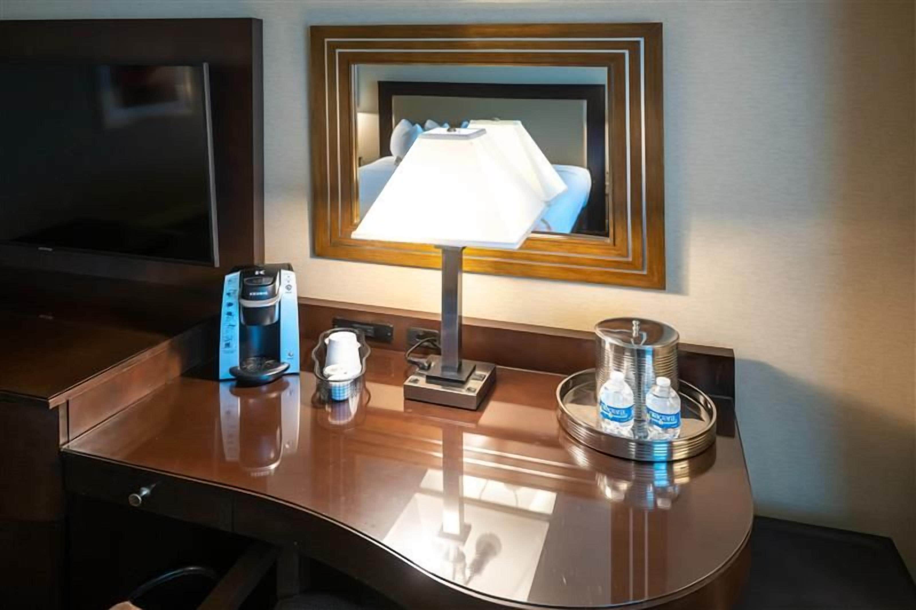 Une chambre d’hôtel équipée d’un téléviseur à écran plat, d’une machine à café, d’une lampe, d’une tasse et d’un plateau avec des bouteilles d’eau.