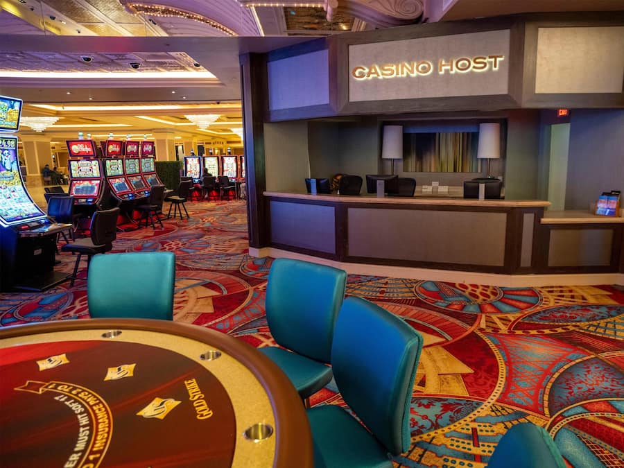 A casino area with slot machines, a roulette table, and a reception desk labeled "CASINO HOST".