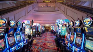 Ein Casino-Bereich mit mehreren Spielautomaten, Rolltreppen und einem Teppichboden.