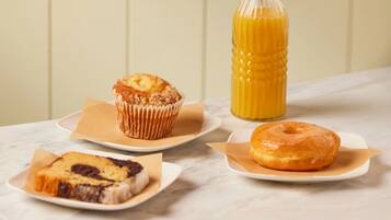 A marble countertop with a muffin, a donut, and a slice of cake on separate plates, and a glass bottle of orange juice.